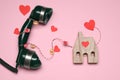 Decorative cord and paper hearts between telephone receiver and wooden house model on pink background Royalty Free Stock Photo