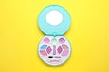 Decorative cosmetics for kids. Eye shadow palette with lipstick on yellow background, top view