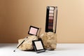 Decorative cosmetics kit. Palette of eyeshadow, pink blush, highlighter and make-up brush on stone. Cosmetic products on beige and Royalty Free Stock Photo