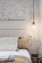 Decorative detail of a bedroom with a white painted wooden headboard, common incandescent lamp socket and fabric cushions