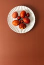 Decorative Easter eggs in various shades of red and orange sit on a white plate on a brown background, showcasing Royalty Free Stock Photo