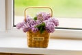 Decorative flower basket with branches of spring lilacs on the windowsill of a country house. the concept of a good spring mood