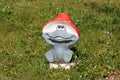 Decorative garden ornament shaped like funny smiling children toy frog with bright red mushroom hat surrounded with uncut grass Royalty Free Stock Photo