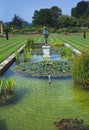 A decorative garden pool with water lilies and a classicl statue in the centre of a large lawn