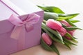 Decorative gift box with purple ribbon and tulips on light background