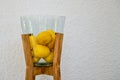 Decorative glass bowl or vase with wooden feet filled with fresh lemons against white wall background