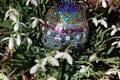 Decorative handicraft sequin Easter egg among snowdrop flowers