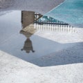 Decorative historic metal fence reflected in puddle after rain, blue block pavement