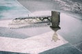 Decorative historic metal fence reflected in puddle after rain, blue block pavement