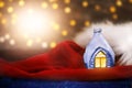 Decorative ice house on Santa Claus`s red velvet hat with fur. Blurred lights with lens flare. Christmas, New Year postcard. Copy Royalty Free Stock Photo