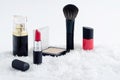 Decorative luxury cosmetics, red lipstick, powder, brush, nail polish and perfume on snow background