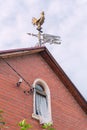 Decorative metal weather vane in the form of a rooster on the roof of the house as a symbol of dawn