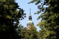 Decorative old church bell tower covered with light green metal with tall cross on top surrounded with dense tree branches Royalty Free Stock Photo