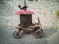 Decorative Pink Flowers in a Big Wooden Vase with an Antique Metallic Instrument inside an Old Wooden Trolley with Wheels