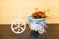 Decorative plastic tricycle with a beautiful basket, bow and flowers standing on a brown shelf. Interior design Royalty Free Stock Photo