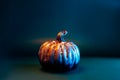 Decorative pumpkin with sparkles in neon warm orange and blue light on the dark green, turquoise surface. Halloween