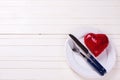 Decorative red heart, knife and fork on white plate on white w