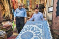 Decorative textiles in city bazaar, Iranian seller demonstrates