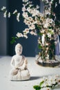 Decorative white Buddha statuette with blooing tree branches in the vase on the dark background. Meditation and Royalty Free Stock Photo