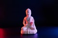 Decorative white Buddha statuette on the dark background in red and blue neon light. Duality concept, Yin Yang. internal Royalty Free Stock Photo