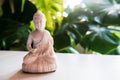 Decorative white Buddha statuette with green monstera plant on the background. Meditation and relaxation ritual. Exotic Royalty Free Stock Photo