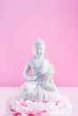 Decorative white Buddha statuette sitting on the peony flower pillow altar on the pink background. Meditation and Royalty Free Stock Photo