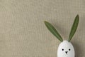 Decorative White Painted Easter Egg Bunny with Drawn Cute Kawaii Face. Green Leaves Ears. Beige Linen Fabric Background Royalty Free Stock Photo