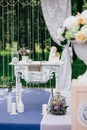 Decorative white vintage table at the wedding ceremony, candle-decorated books with flowers and ceramic angles and a