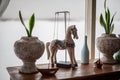 Decorative wooden horse stands on the table near the window flowers in pots, white bottle, iron boat, elements of room decoration, Royalty Free Stock Photo
