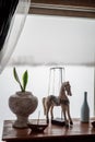 Decorative wooden horse stands on the table near the window flowers in pots, white bottle, iron boat, elements of room decoration, Royalty Free Stock Photo