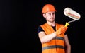 Decorator painting wall, copy space. Man in helmet, hard hat holds paint roller, black background. Worker, painter Royalty Free Stock Photo