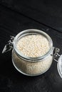 Decorticated sesame seeds, in glass jar, on black wooden background