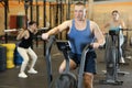 Dedicated active strong middle-aged man doing cardio workout on stationary bicycle as hard cross-training in gym indoors Royalty Free Stock Photo