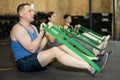 Motivated man practicing exercises with stretch rope sitting near other people in gym Royalty Free Stock Photo