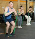 Motivated man practicing exercises with stretch rope standing near other people in gym Royalty Free Stock Photo