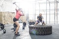 Dedicated man and woman hitting tire with sledgehammer in crossfit gym