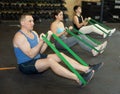 Motivated man practicing exercises with stretch rope sitting near other people in gym Royalty Free Stock Photo