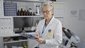 Dedicated senior grey-haired scientist woman, in lab coat, taking intricate notes at center\'s laboratory amidst science research Royalty Free Stock Photo