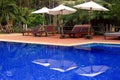 Deep blue and calm pool with some wooden beach-benchs and white umbella in tropical style resort.