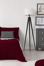 Deep burgundy cover on a bed standing next to a modern black and white lamp in a contemporary bedroom interior. Real photo. Royalty Free Stock Photo