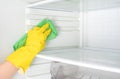 Hand cleaning refrigerator. Person washing refrigerator with rag. Housekeeper wipes shelves of clean refrigerator. Hand in yellow Royalty Free Stock Photo
