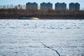 A deep crack in the ice of the river in front of the ice drift. Spring landscape. Forest and residential buildings on Royalty Free Stock Photo