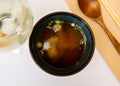 In deep dark bowl, portion of miso vermicelli soup with addition of young onion greens.