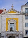 Deep, egg-yolk yellow historic building with stone framed French door, balcony, and deep blue sky in Lisbon, Portugal.