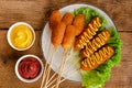 Deep fried corn dogs with mustard and ketchup on wooden background. American junk food concept.