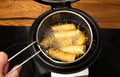 Deep fried fritted vegetable spring rolls inside special deep fryer electrical machine pot, boiling in hot cooking oil.