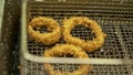 Deep fried onion ring. Oniony Rings cooking in hot bubbly oil in a deeped fryer. Golden chopped onions circle frying