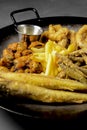 Deep fried set made from french fries, onion rings, big and small fried fish served in a wok over black background. Royalty Free Stock Photo