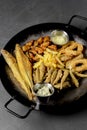 Deep fried set made from french fries, onion rings, big and small fried fish served in a wok over black background. Royalty Free Stock Photo
