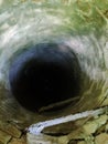 A deep hole in an underground sewage collector with rusty stairs and moldy walls